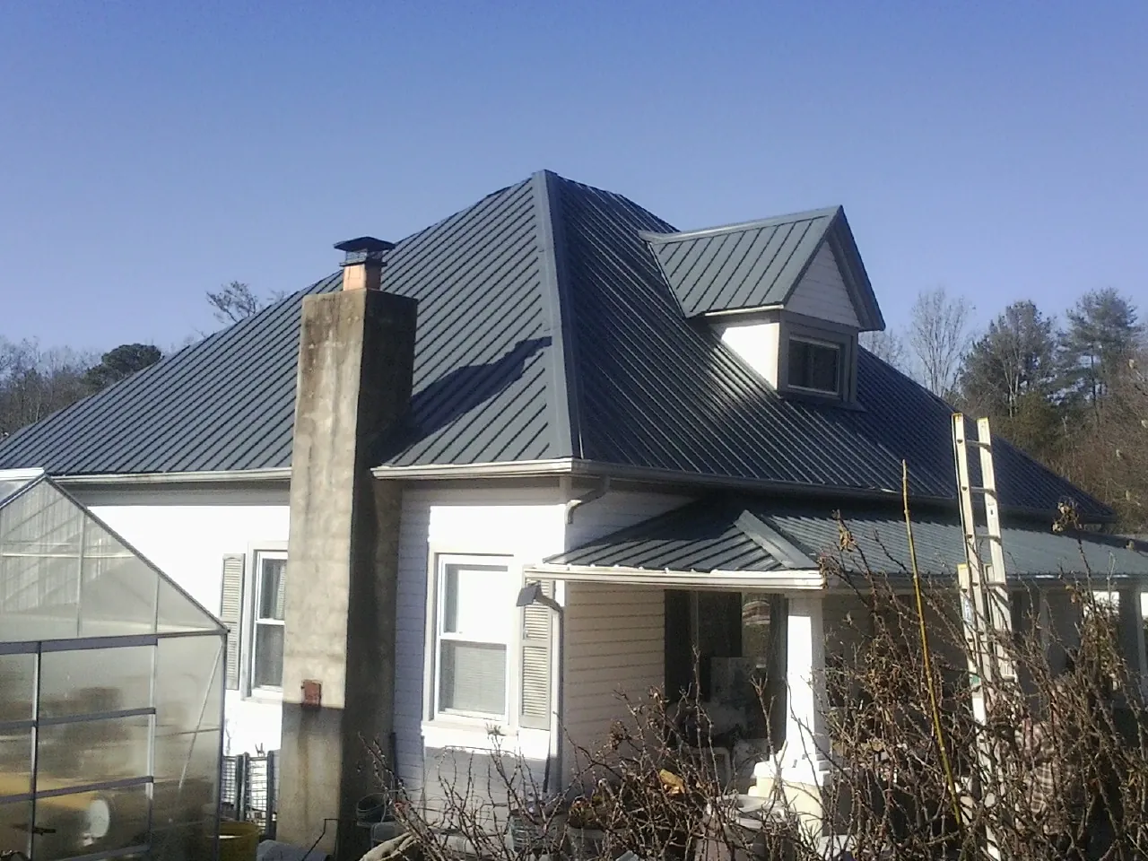 Dark blue standing seam metal roof on a white farmhouse with dormer — Slate & Tile Roof Repair by Roofing Brothers in Haslet