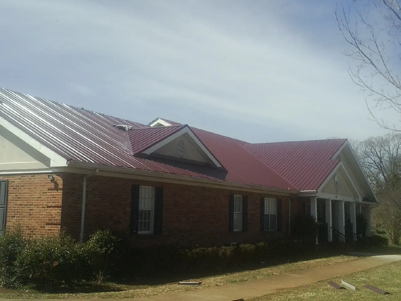 Red metal roof with gabled entries on a long brick building, from a Hail Damage Roof Repair job in Haslet