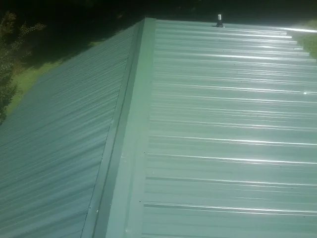 New green metal panels meeting at the ridge of a roof — Flat Roof Repair work by our crew in Haslet