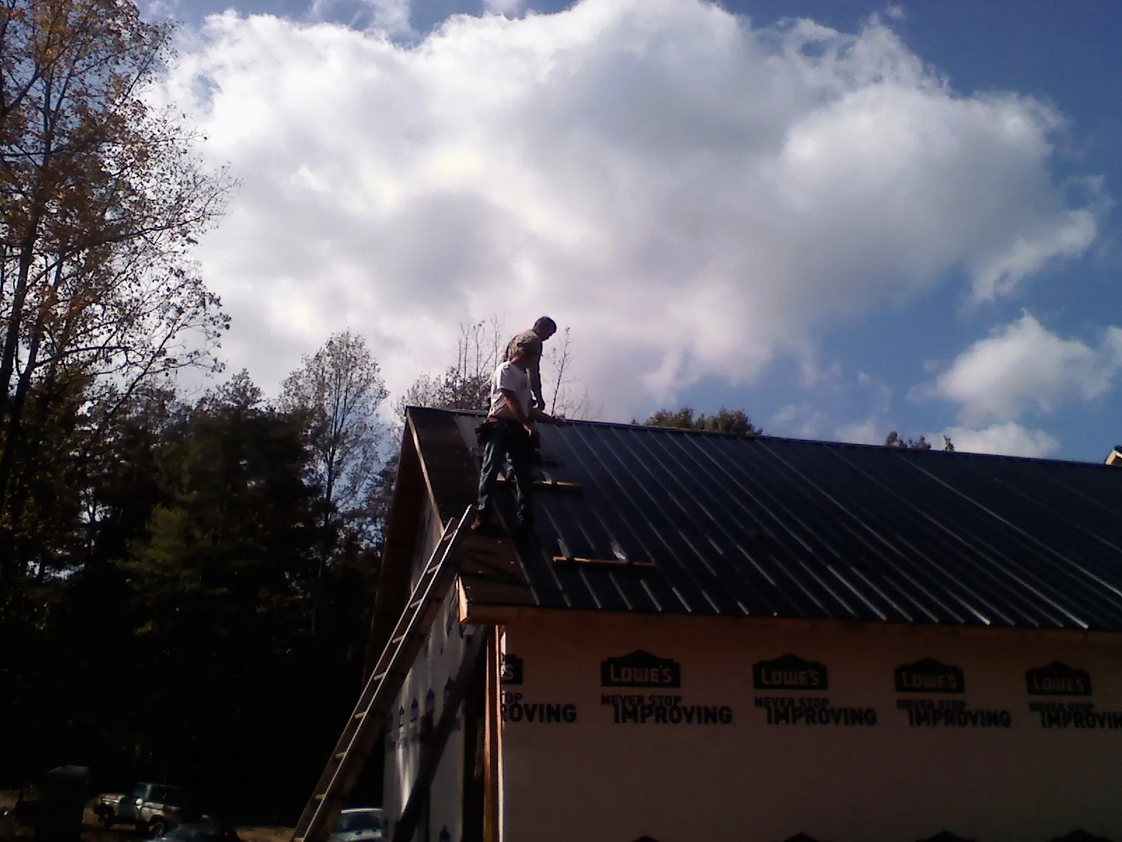 Roofer fastening dark metal panels high against a cloudy sky, from a Roof Inspection job in Haslet