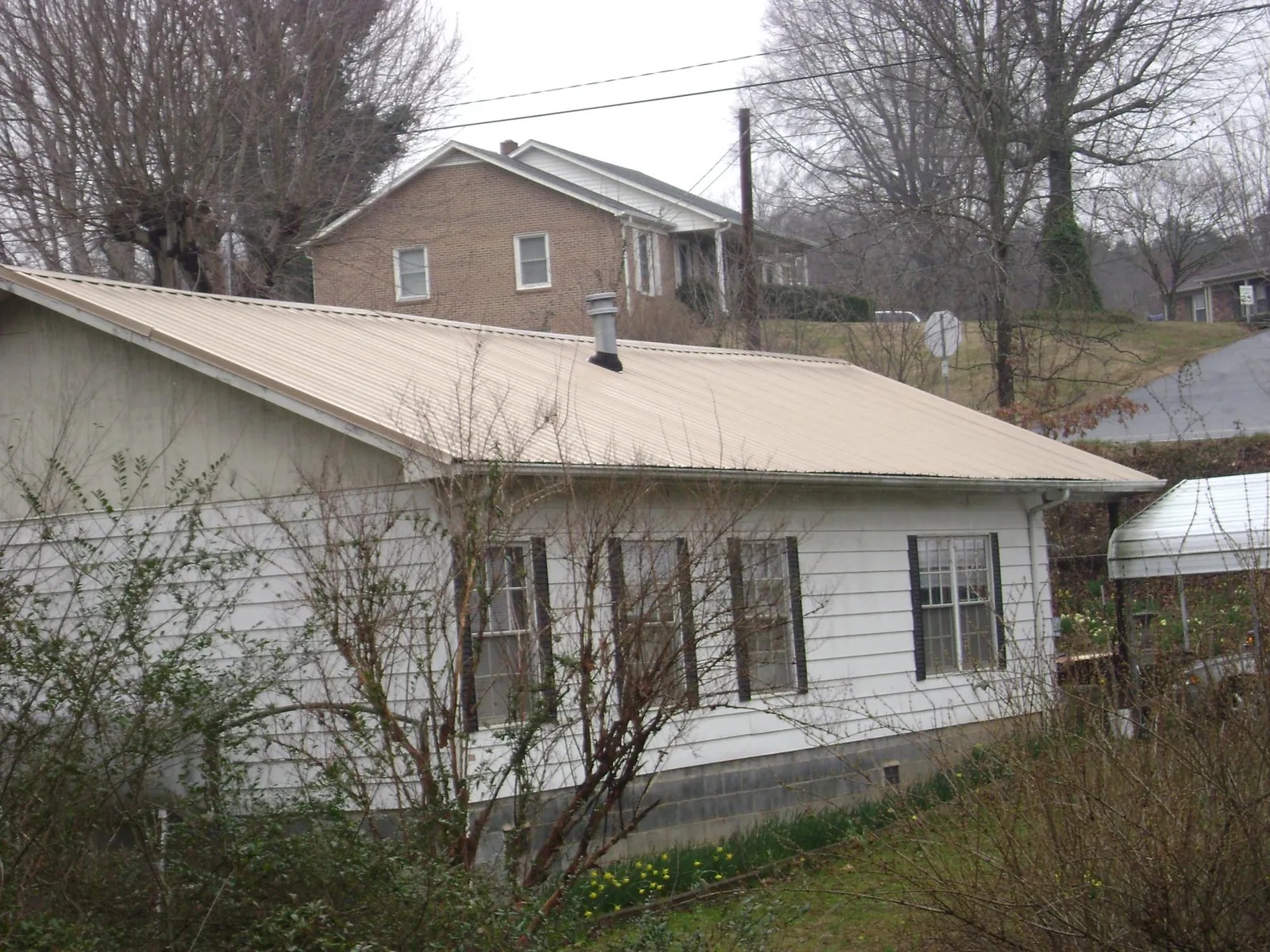 Tan metal roof on a white sided house set into a hillside — Commercial Roofing by Roofing Brothers in Haslet