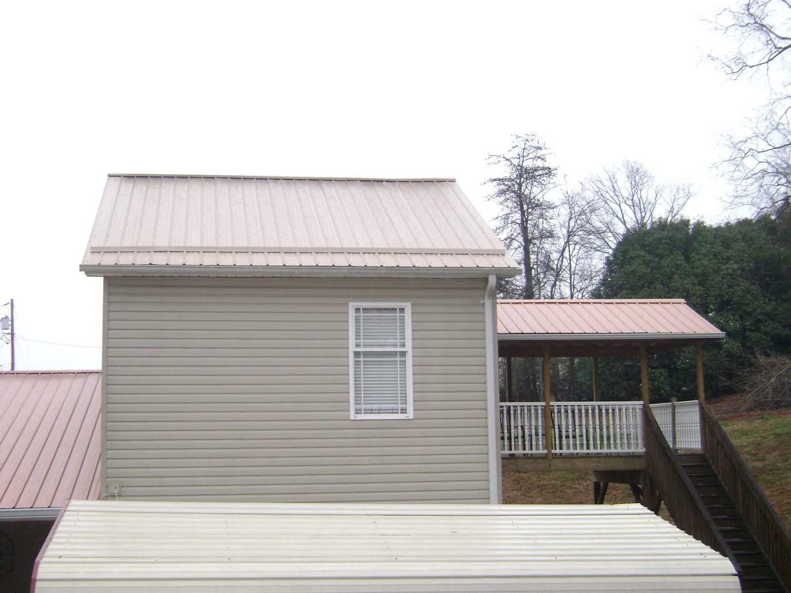 Tan metal roofs on a two story addition and attached porch, from a Roof Replacement job in Haslet